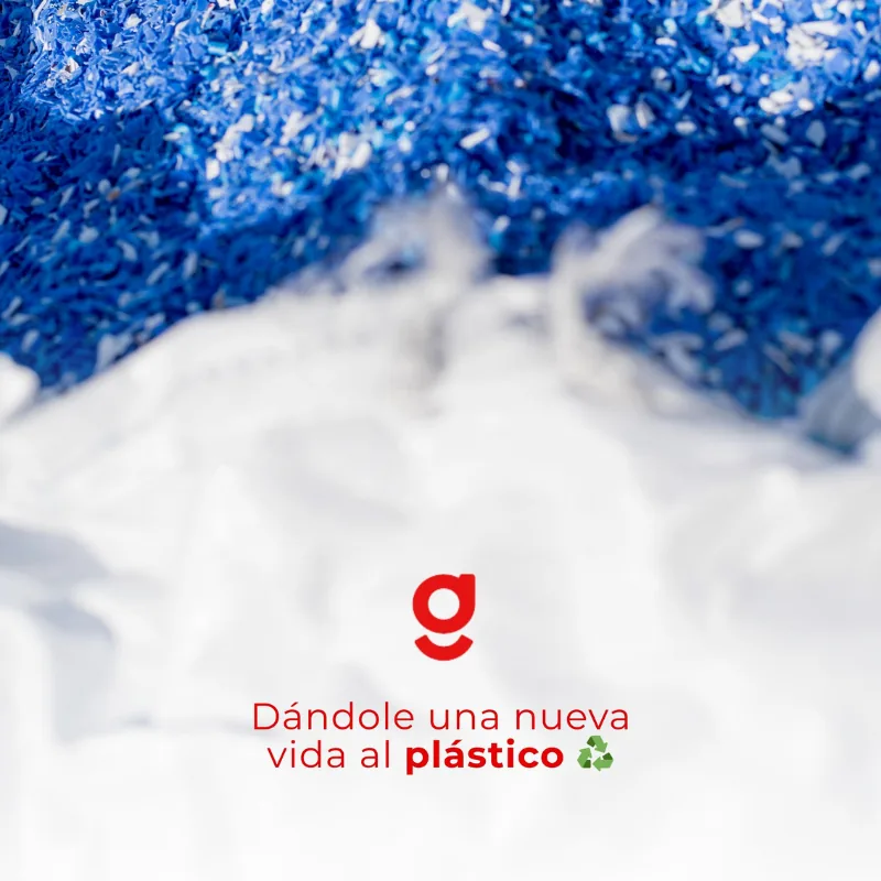 Detalle de las escamas de plástico molido, azules y blancas, listas para reprocesar. Sobre la foto, la leyenda «Dándole una nueva vida al plástico»