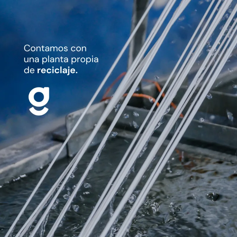 Hilos de material recuperado saliendo de la extrusora hacia la pileta de enfriado. Sobre la foto, la leyenda «Contamos con una planta propia de reciclaje»